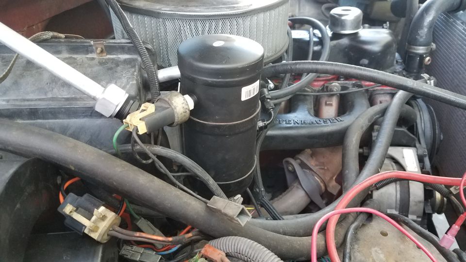 Close-up of 1985 Ford Bronco engine bay showing AC receiver-drier, hoses, and wiring.