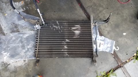 1985 Ford Bronco - A car's air conditioning condenser unit is laid out on a concrete surface. The unit has two hoses attached and a part number tag reading "5…