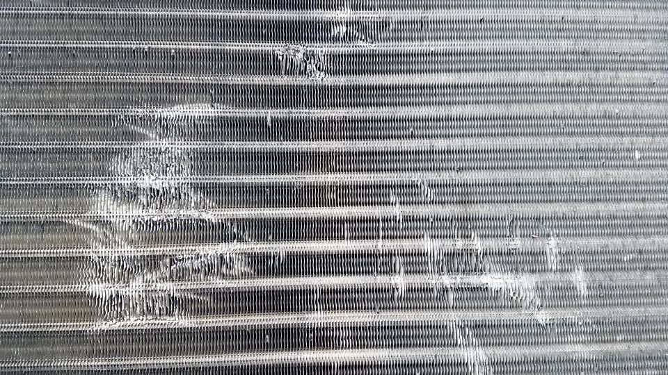 Close-up of a damaged condenser coil with bent fins