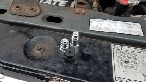 1985 Ford Bronco - Several automotive air conditioning service adapters and caps are laid out on the engine bay of a vehicle. A sticker with vehicle informati…