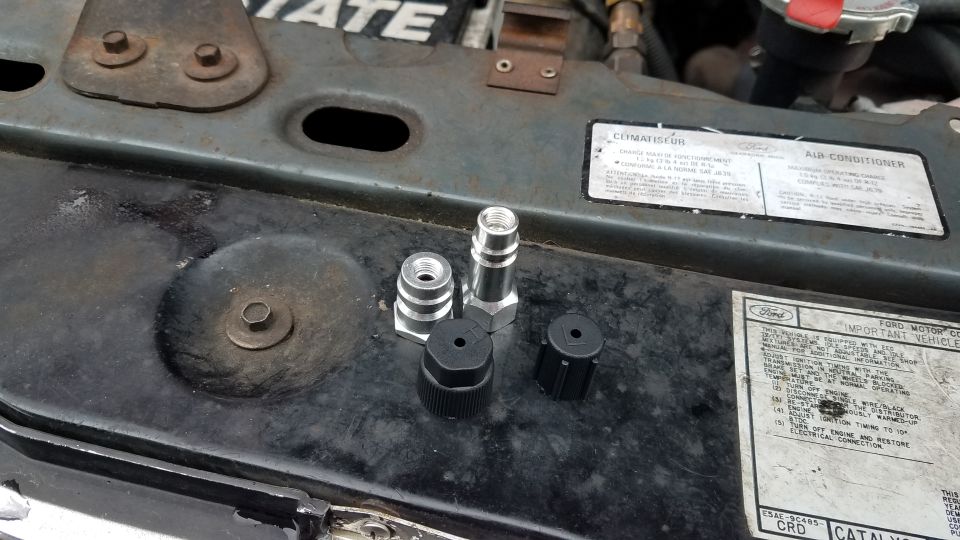 Automotive AC service adapters and caps on a vehicle engine bay.