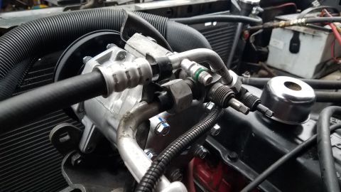 1985 Ford Bronco - A close-up view of a vehicle's engine bay, focusing on the air conditioning compressor and associated hoses connected to the engine block.