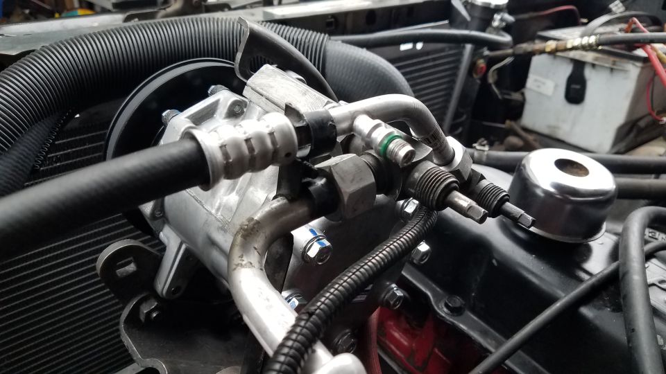 Vehicle AC compressor and hoses connected to engine block.