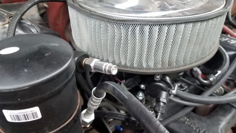 1985 Ford Bronco - A close-up view of the engine bay of a vehicle, focusing on the air filter assembly and a black cylindrical component. A silver fitting wit…