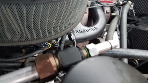1985 Ford Bronco - A close-up view of engine components in a vehicle, featuring a black air filter housing and a black intake manifold with the embossed text…