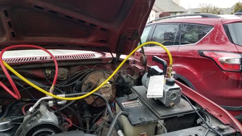 1985 Ford Bronco - The engine bay of a red Ford Bronco is open, with a vacuum pump connected to the air conditioning system via red and yellow hoses. A red SU…