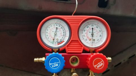 1985 Ford Bronco - A red manifold gauge set with two pressure gauges, labeled "LOW" and "HIGH" with blue and red knobs respectively, is shown in front of a da…