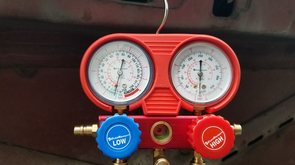 Red manifold gauge set with two pressure gauges, LOW and HIGH knobs.