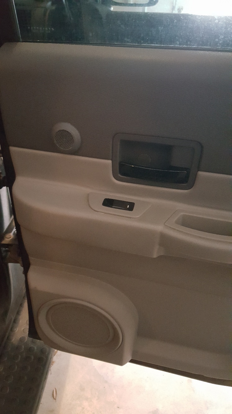 Interior door panel of a vehicle with speakers, door handle, and window switch.