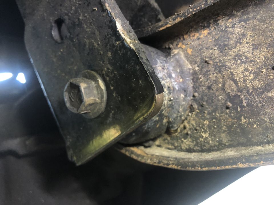 Close-up of a corroded metal bracket with a hex bolt on a vehicle frame.