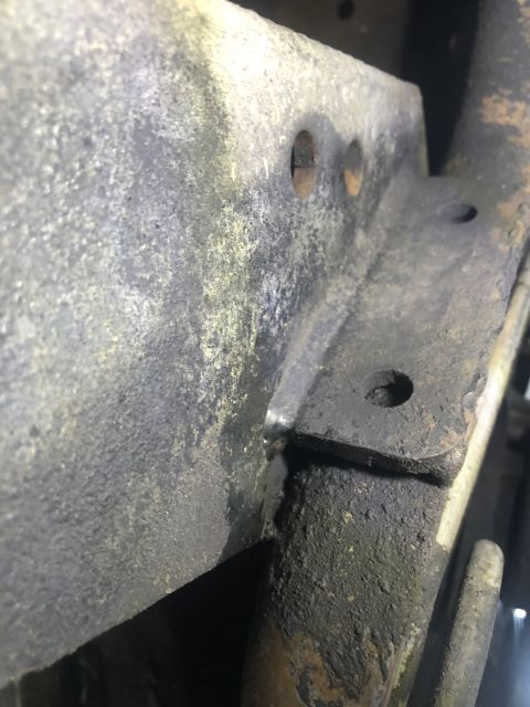 1995 Ford Bronco - A close-up, low-angle shot shows a rusted and greasy metal bracket attached to a vehicle frame. The bracket has several bolt holes and appe…