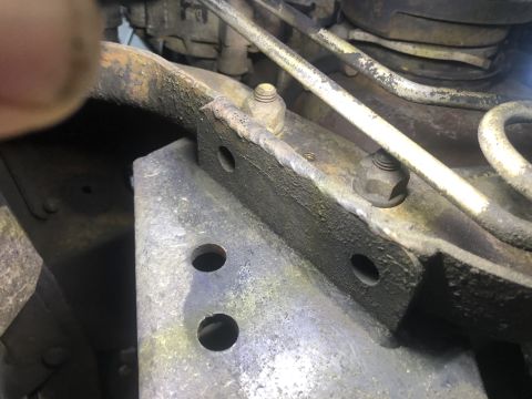 1995 Ford Bronco - A close-up view shows a rusty metal bracket attached to a vehicle frame, secured by bolts and nuts. Metal tubing and other components are v…