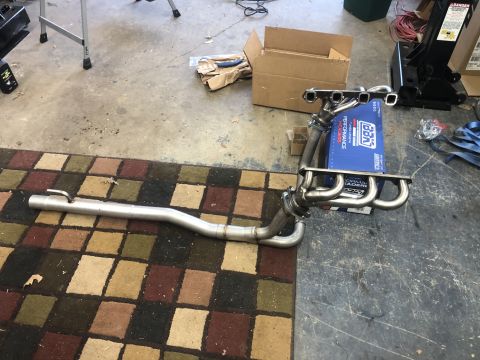 1995 Ford Bronco - A set of chrome exhaust headers and a section of exhaust pipe are laid out on a checkered rug. A blue box with "BBK PERFORMANCE" text is vi…