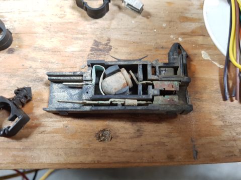 1978 Ford Bronco - A disassembled electrical component, possibly a fuse box or relay, sits on a wooden surface. Wires are visible to the right, and other blac…