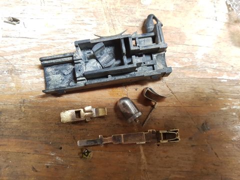 1978 Ford Bronco - Disassembled electrical connector components are laid out on a wooden surface. A black plastic housing is at the top, with brass and metal…