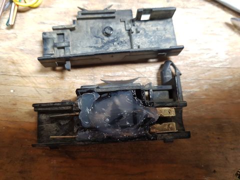 1978 Ford Bronco - Two disassembled black plastic electrical components are shown on a wooden surface. The bottom component has a large blob of clear, viscous…