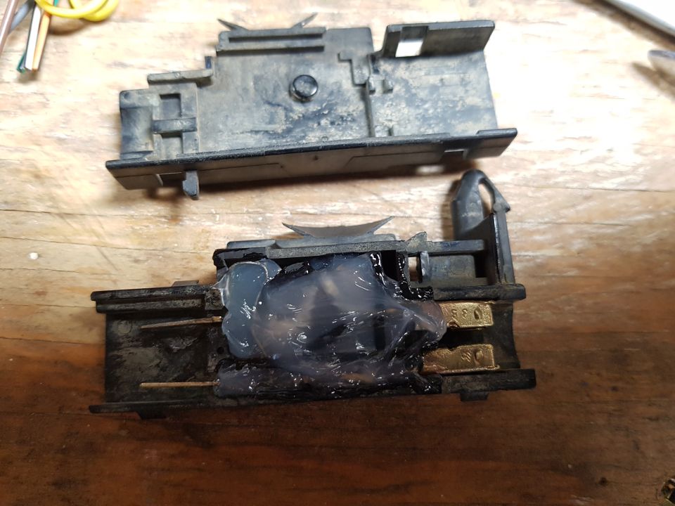 Two disassembled black plastic electrical components with internal metal contacts, one covered in clear gel.