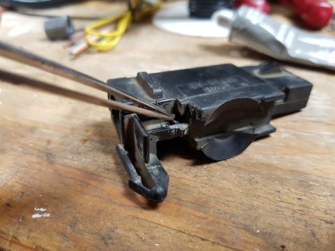 1978 Ford Bronco - Tweezers are used to manipulate a black plastic electrical component, possibly a sensor or switch, resting on a wooden surface. The compone…