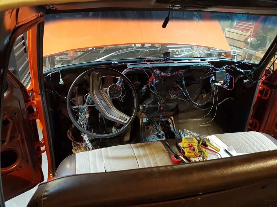 1978 Ford Bronco interior with dashboard wiring exposed, orange exterior, brown and white seats, and tools on the seat