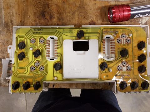 1978 Ford Bronco - The backside of a vehicle's instrument cluster circuit board is shown, resting on a wooden surface.