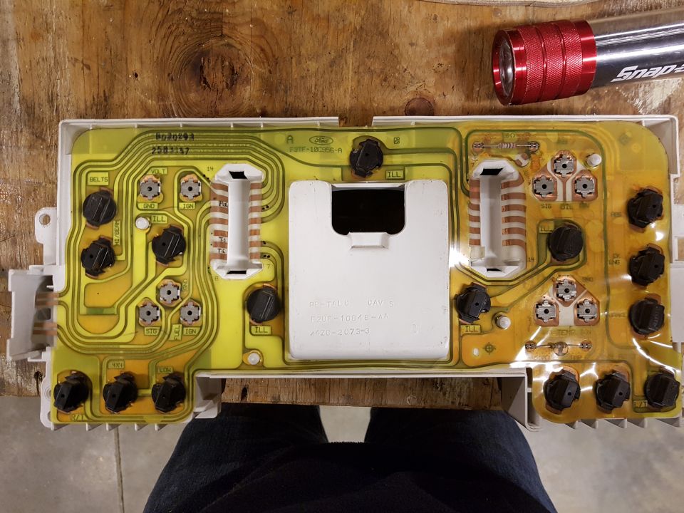 Back of a vehicle's instrument cluster circuit board with a red Snap-on flashlight nearby