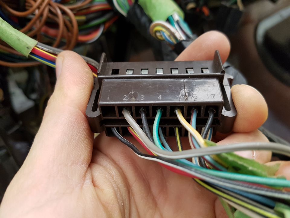 Hand holding a brown electrical connector with numbered pins and multiple colored wires