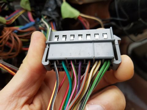 1978 Ford Bronco - A hand holds a gray wiring harness connector with numerous colored wires attached.