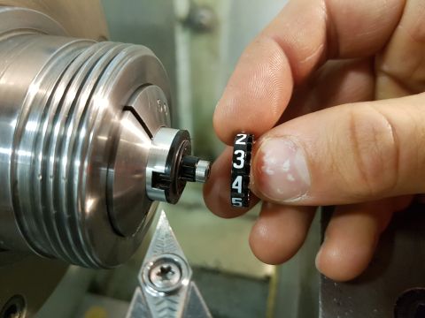 1978 Ford Bronco - A gear shift knob insert with numbers 2 through 5 is held near a metal lathe.