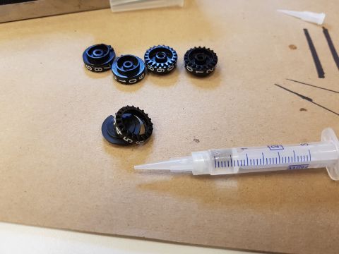 1978 Ford Bronco - Several black knobs with numerical markings and a syringe filled with liquid are laid out on a textured surface.