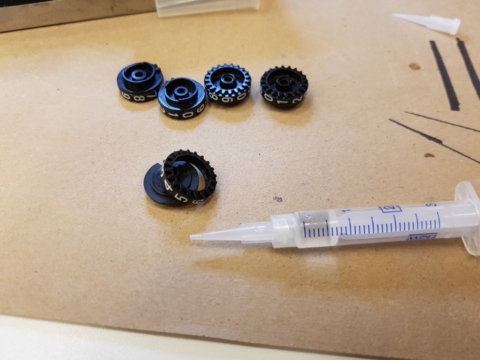 Black knobs with white numbers and a syringe with liquid on a brown surface