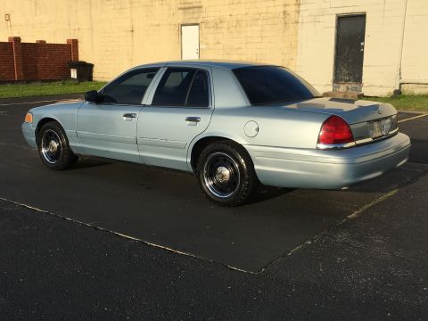 2006 Ford Crown Victoria - A light blue 2006 Ford Crown Victoria is parked on asphalt in front of a building with a brick wall.