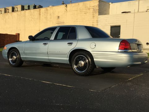 2006 Ford Crown Victoria - A light blue 2006 Ford Crown Victoria sedan is viewed from the rear quarter angle, parked on asphalt.