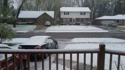 Snow covers cars parked in driveways and on a street in front of suburban houses