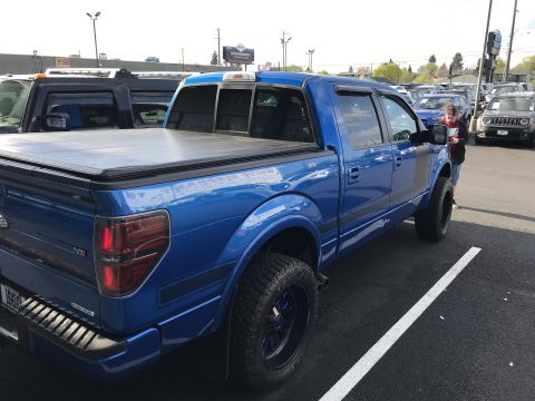 2013 Ford F-150 - This blue pickup truck features black racing stripes and aftermarket wheels, offering a distinctive look from its rear three-quarter perspe…