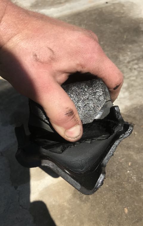 1995 Ford Bronco - A hand holds a severely damaged engine mount, showing the torn rubber and metal components.