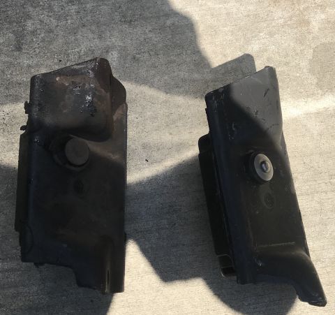 1995 Ford Bronco - Two black metal automotive parts are shown resting on a concrete surface. One part has a visible bolt head.
