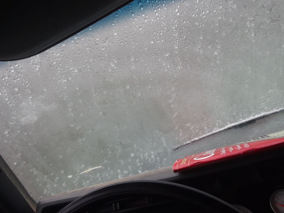 View through a wet windshield with a red object on the dashboard.