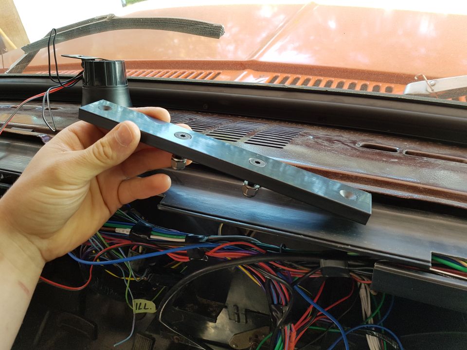 Hand holding a bracket over a car dashboard with exposed wiring.