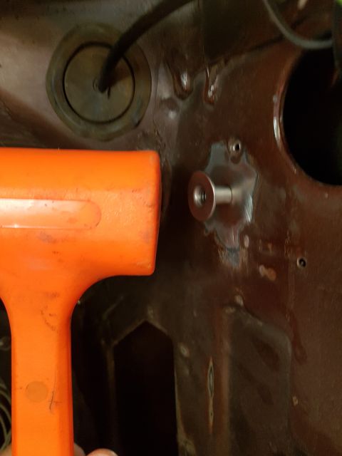 1978 Ford Bronco - An orange mallet is positioned next to a metal bracket with a bolt on a rusted, dark red metal surface. The surface appears to be part of a…