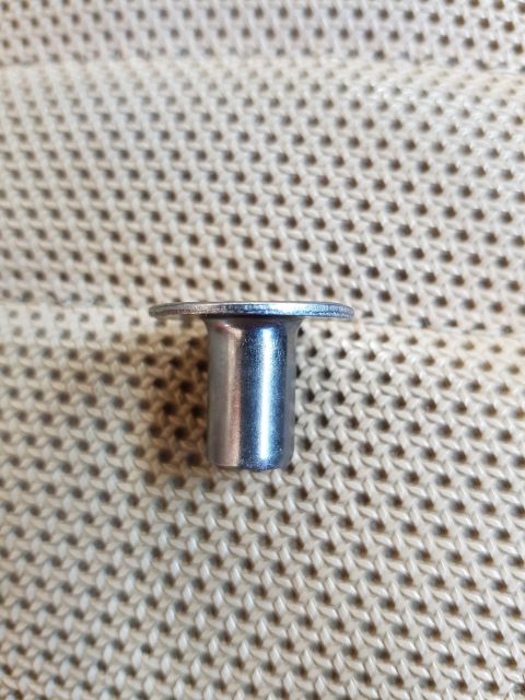 1978 Ford Bronco - A single metal rivet with a flange is shown against a textured, beige background. The rivet is cylindrical with a flared top.
