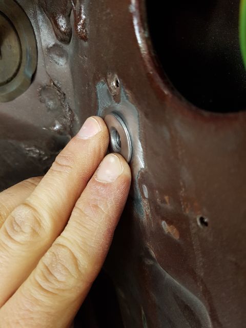 1978 Ford Bronco - A person's fingers are shown holding a metal washer against a dark brown painted metal surface. The surface appears to be part of a vehicle…