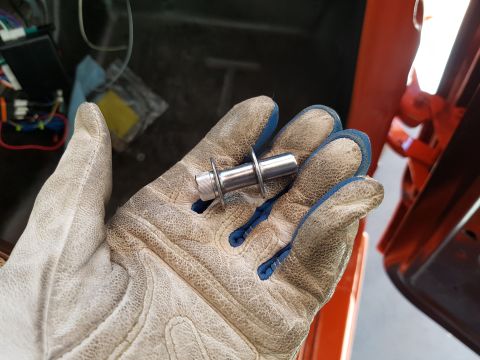 1978 Ford Bronco - A gloved hand holds a metal bolt with a washer and a nut. The background shows a vehicle interior with wiring and orange body panels.