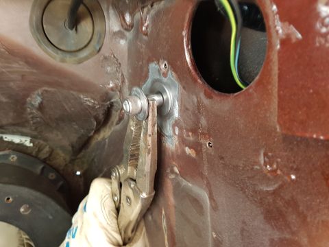 1978 Ford Bronco - A gloved hand uses locking pliers to hold a bolt passing through a rusty metal panel. A black circular grommet with a wire is visible to th…