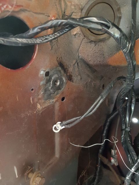 1978 Ford Bronco - A close-up view of a rusted metal surface with a welded nut and a ground wire with a ring terminal attached. Several black wires are bundle…