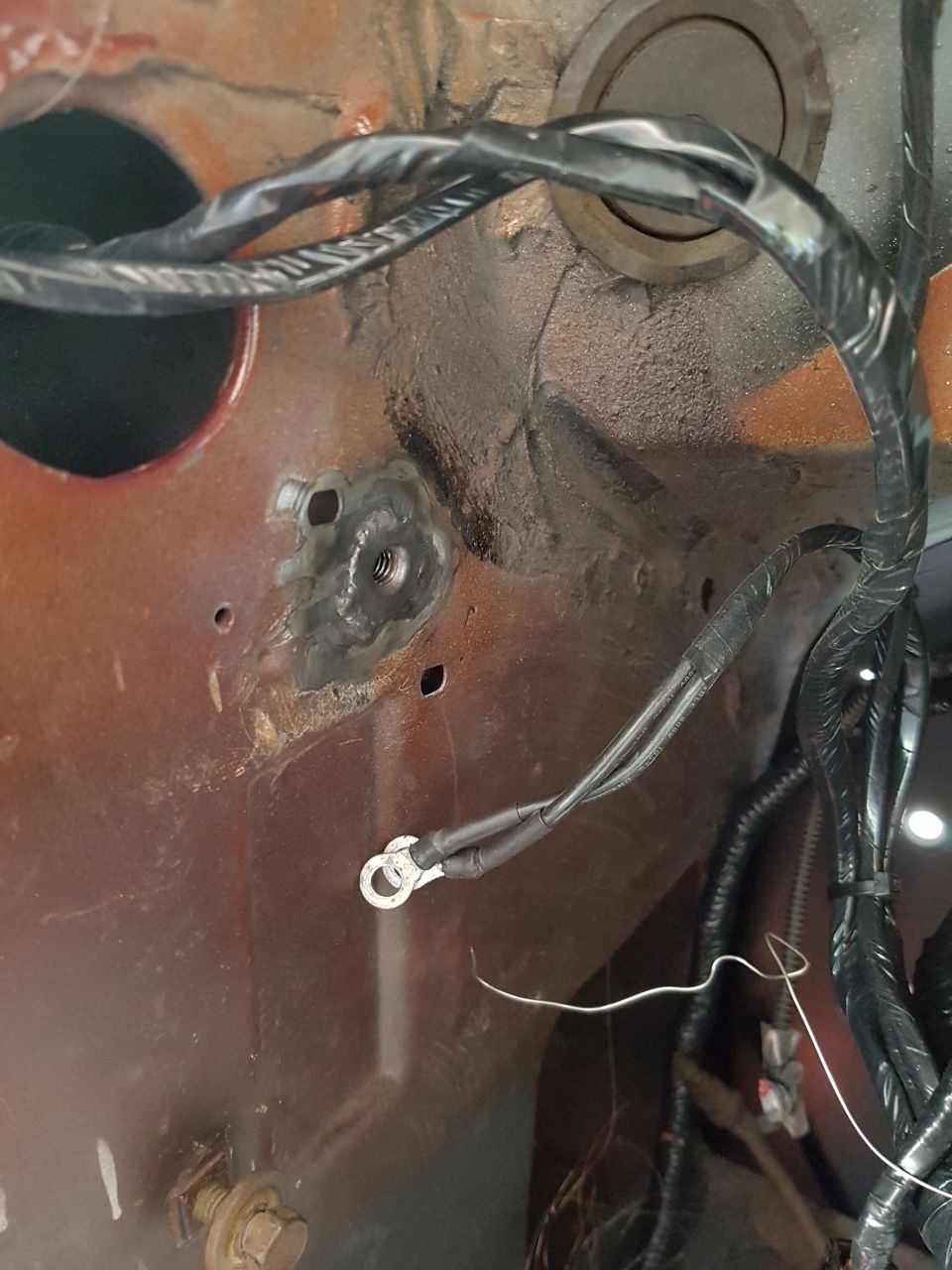 Rusted metal surface with welded nut and ground wire, near bundled black wires.