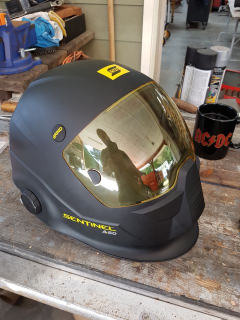 1978 Ford Bronco - A black welding helmet with a gold visor is shown on a wooden workbench. The helmet has yellow branding that reads "ESAB" and "SENTINEL A50…
