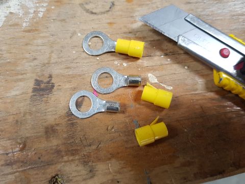 1978 Ford Bronco - Three ring terminals with yellow insulation and a utility knife are scattered on a wooden surface. Some yellow insulation pieces are detach…