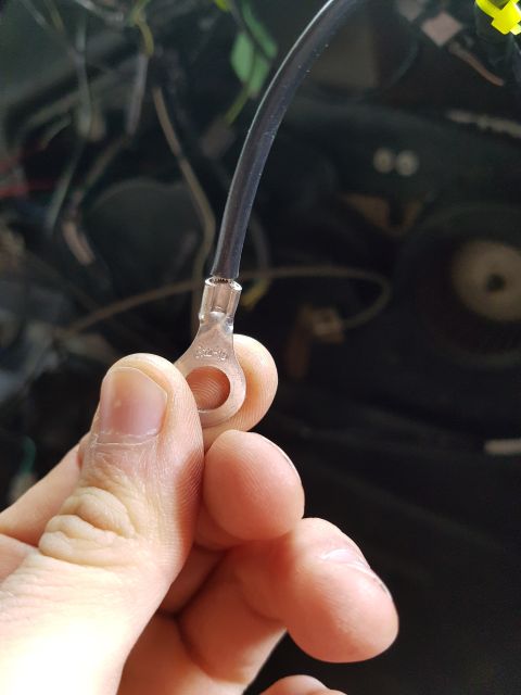 1978 Ford Bronco - A hand holds a black wire with a metal ring terminal crimped onto the end. The terminal has text that appears to read "R2-10". The backgrou…