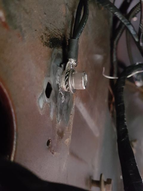 1978 Ford Bronco - A close-up view shows a metal ground lug attached to a vehicle body panel with a bolt and washer. A black wire with white text is connected…