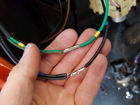 1978 Ford Bronco - A person's hand holds two wires, one green with yellow tape and one black with blue tape, that have been crimped with metal connectors. The…